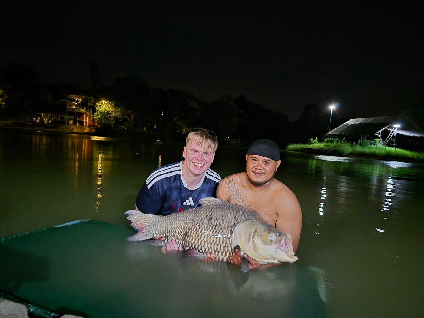 Angler and staff with a giant carp landed at night